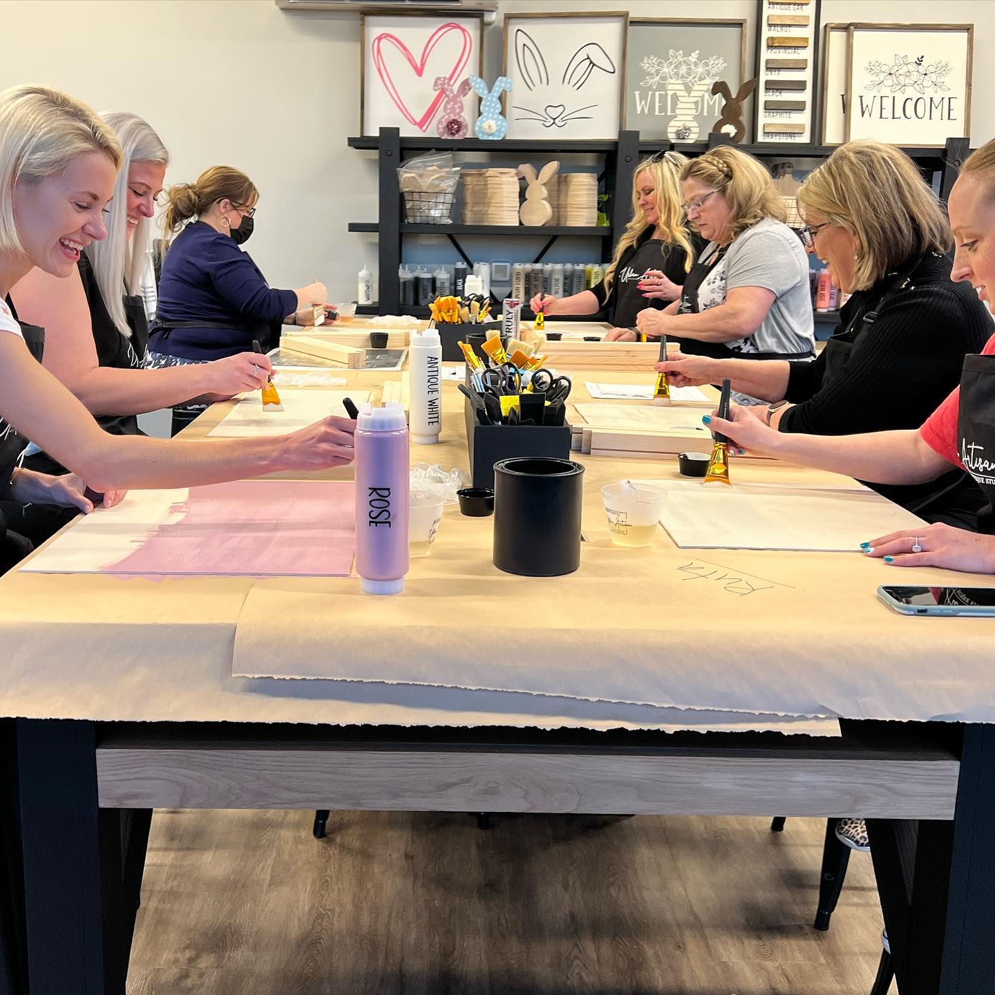 A group of people are sitting at tables in a room with a bottle of purple paint on the table.