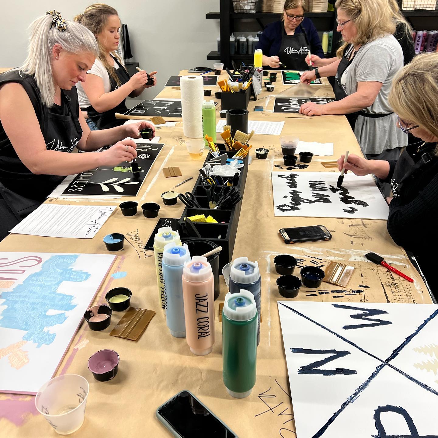 A group of women are sitting at a long table painting.