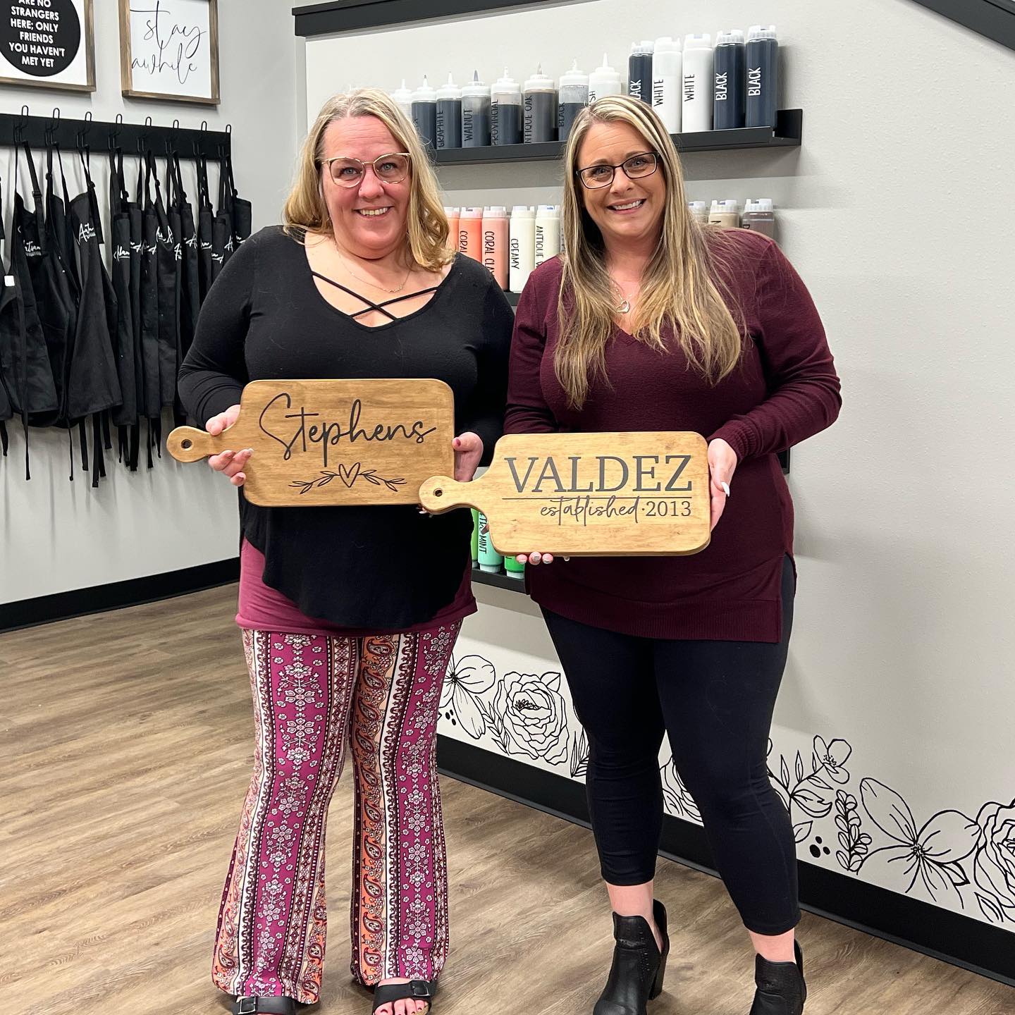 Two women are standing next to each other in a room holding wooden signs.