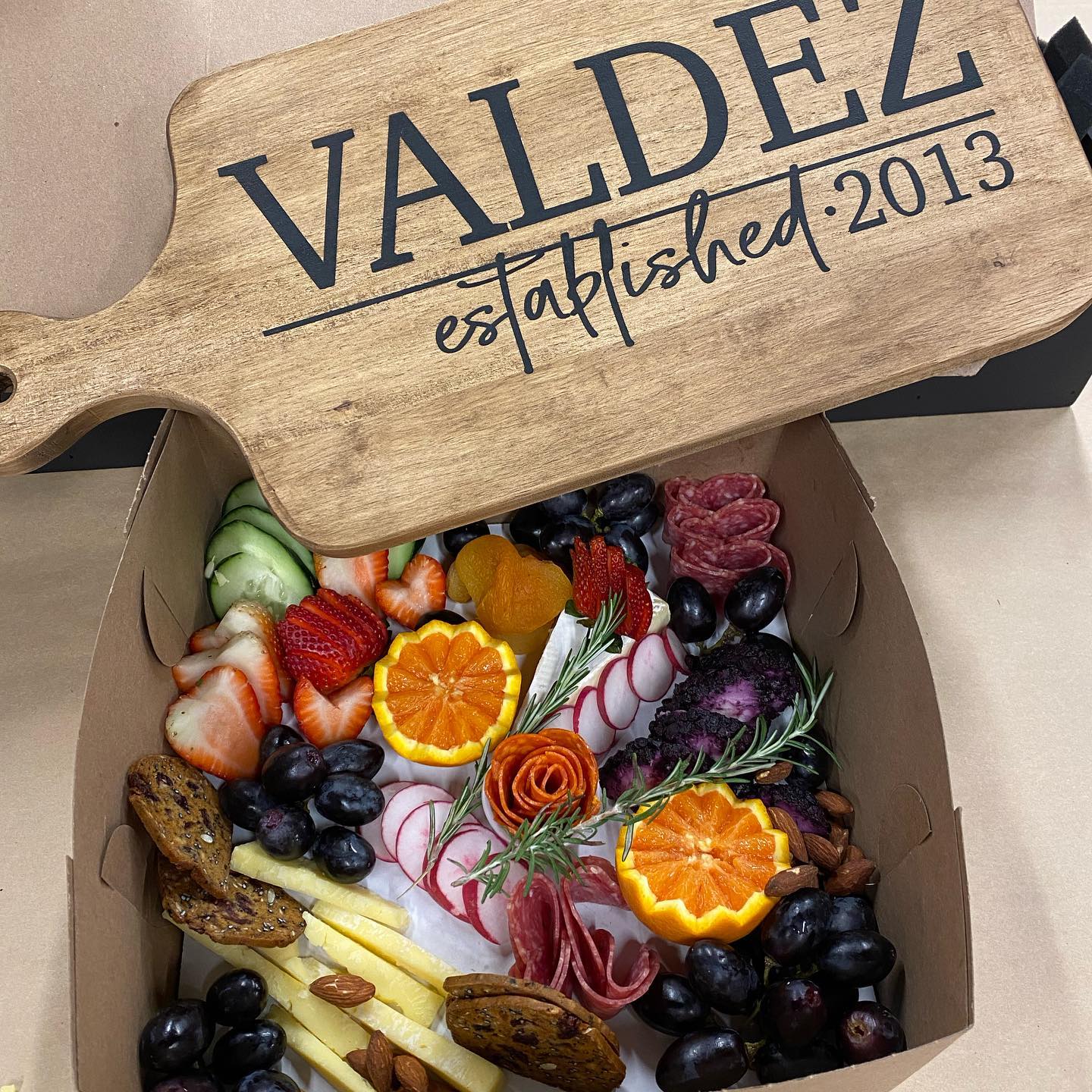 A box of food with a wooden cutting board that says valdez established 2013