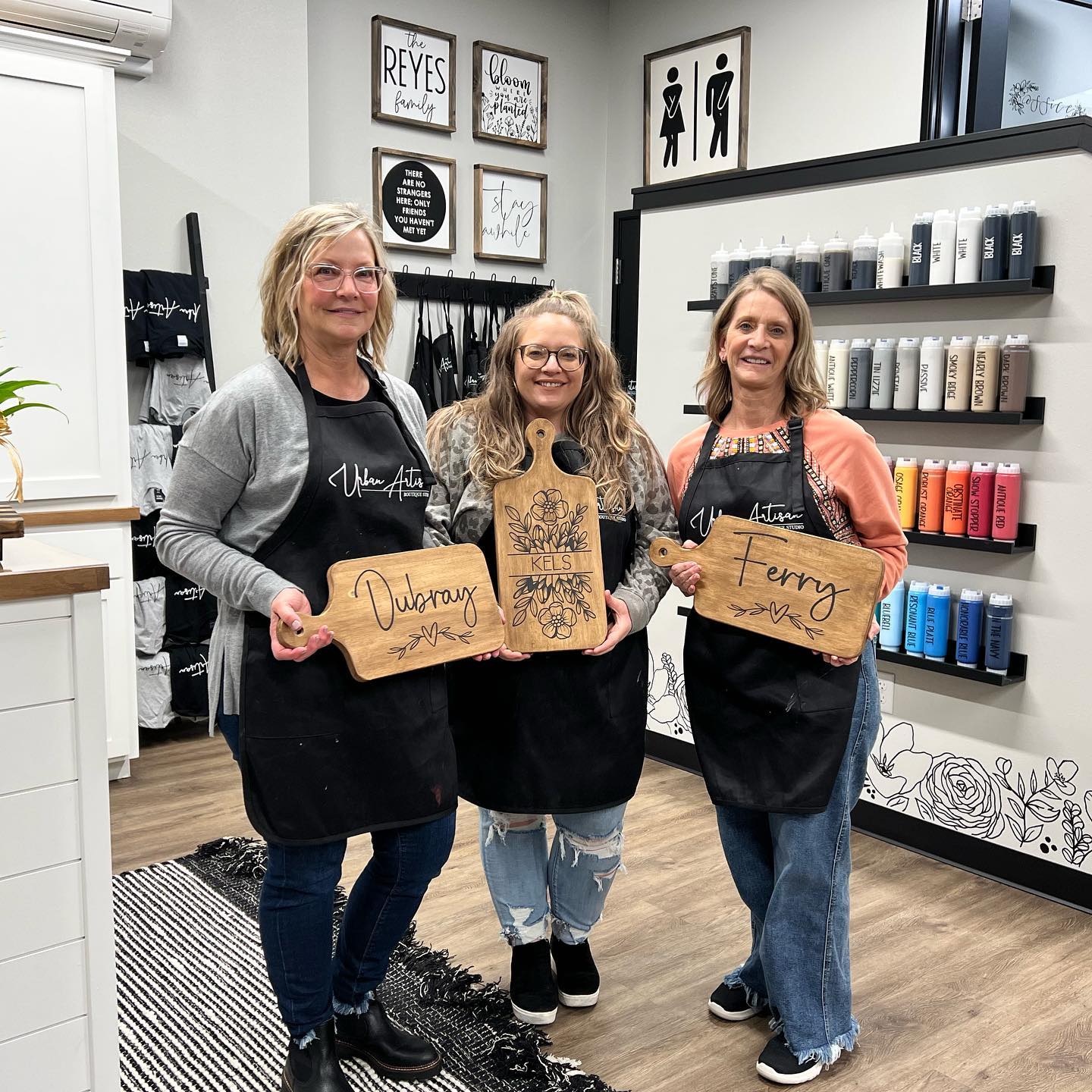 Three women are standing next to each other in a salon holding cutting boards.