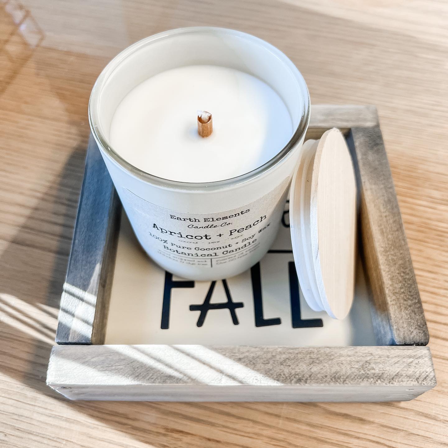 A white candle is sitting on top of a sign that says fall