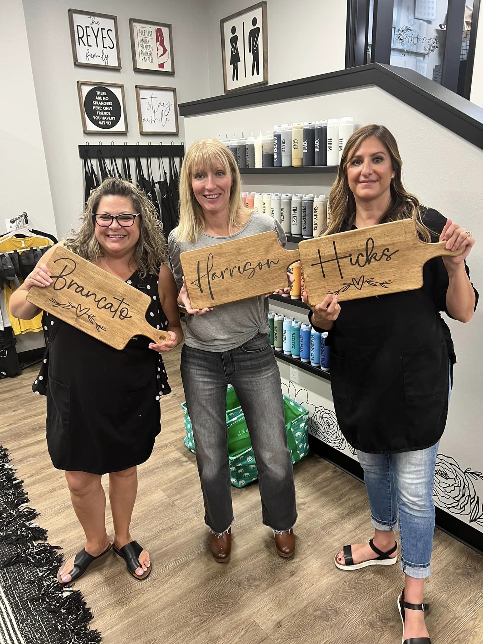 Three women are holding wooden signs in a salon.