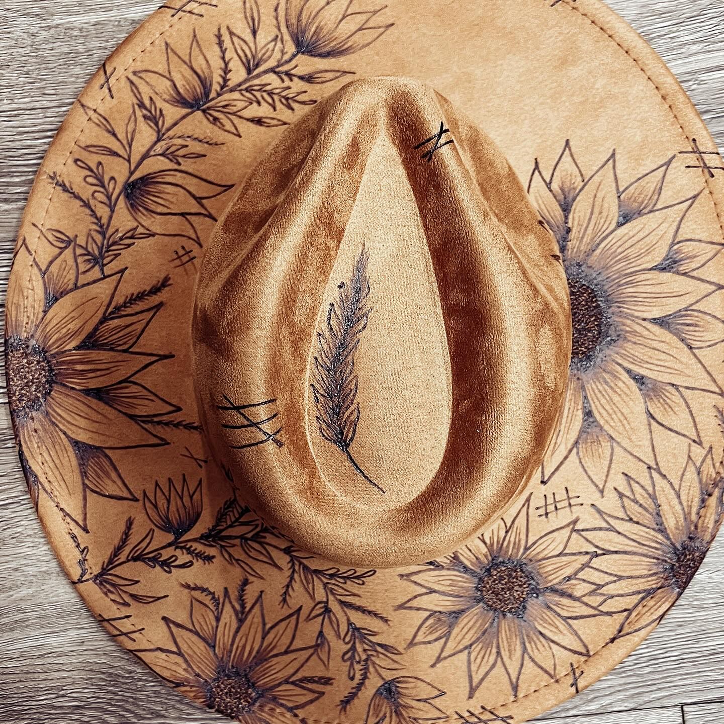 A hat with flowers and feathers painted on it is sitting on a wooden table.