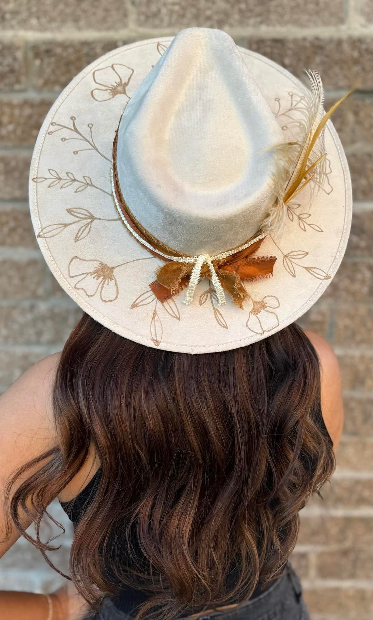 A woman wearing a white hat with feathers on it is standing in front of a brick wall.