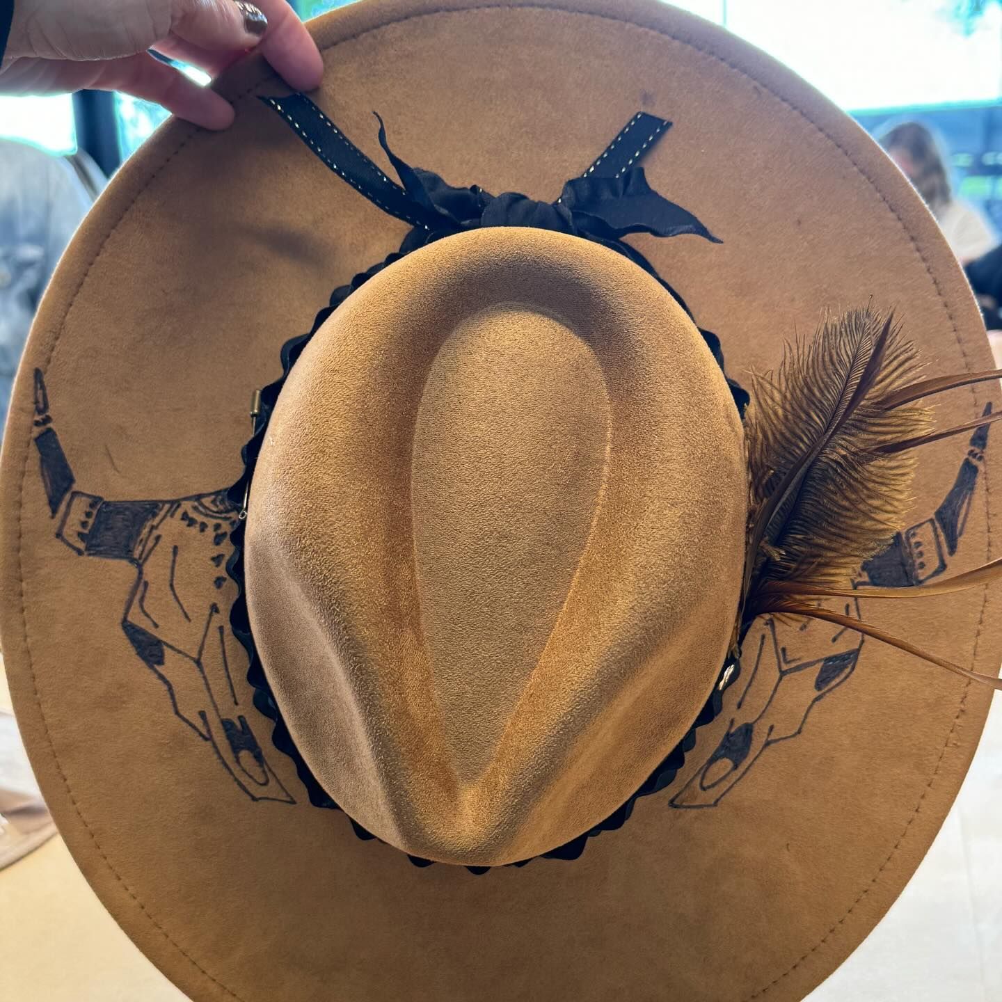 A person is holding a cowboy hat with a feather on it