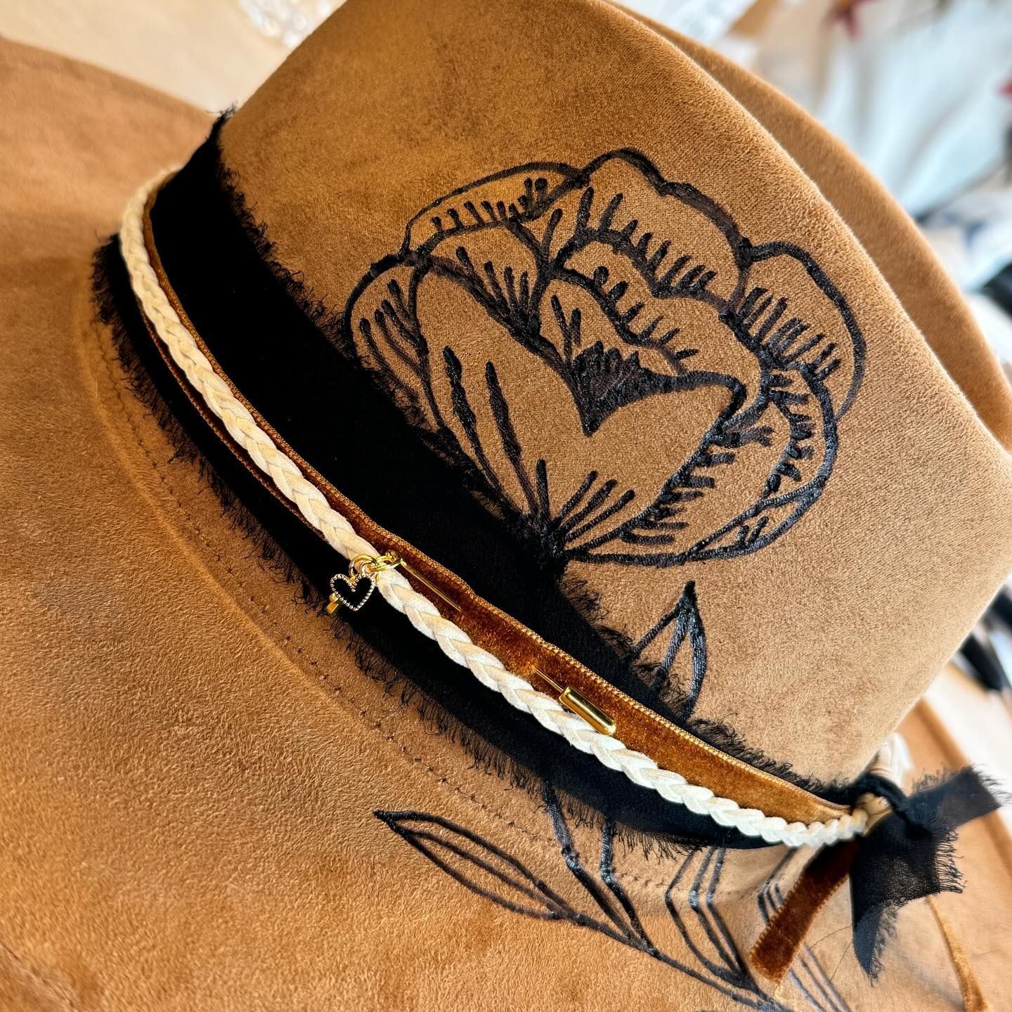 A brown hat with a black flower embroidered on it