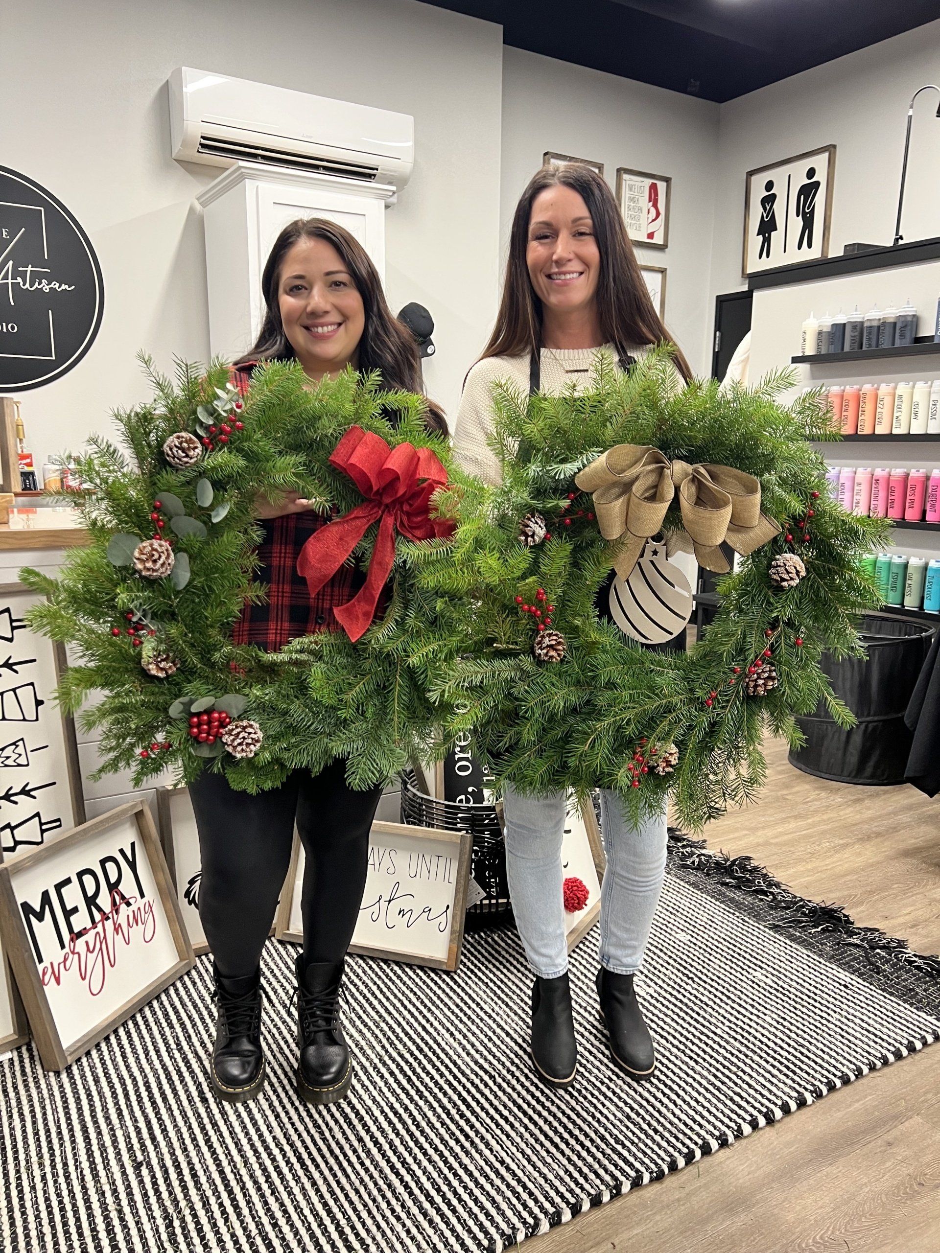 Two women are holding christmas wreaths in a store.