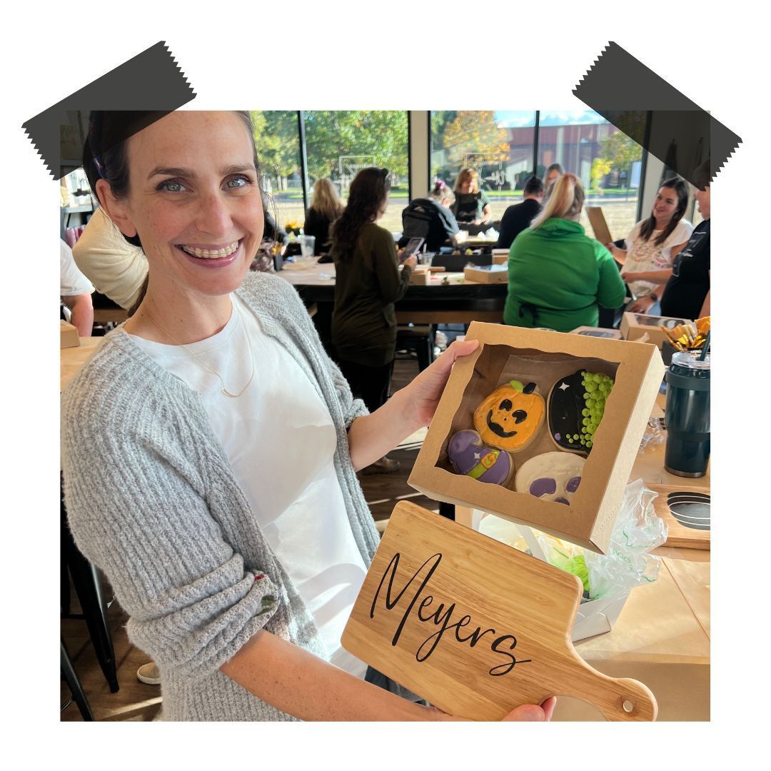 A woman is holding a box of cookies and a cutting board with the name meyers on it.
