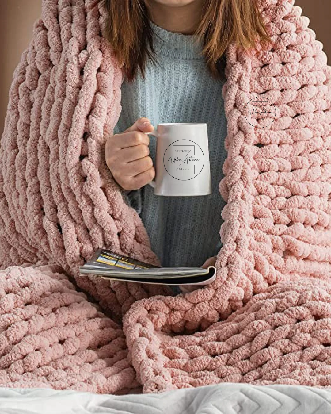 A woman is wrapped in a pink blanket and holding a cup of coffee.