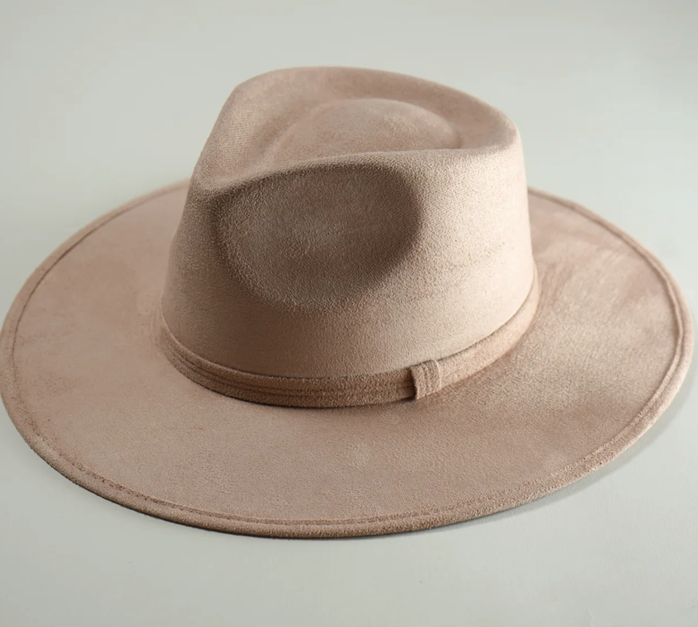 A tan fedora hat is sitting on a white surface.
