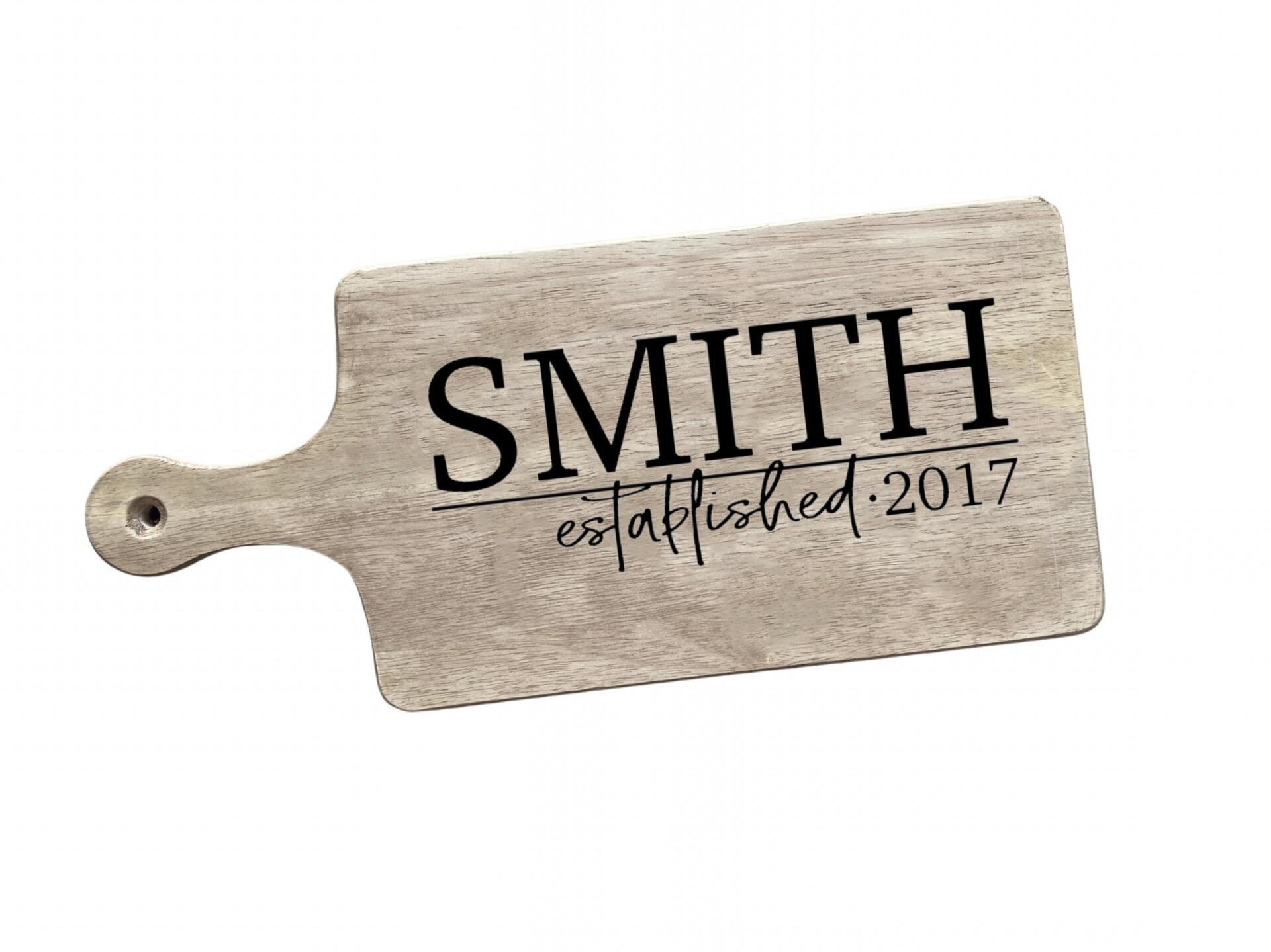 A wooden cutting board with the name smith established 2017 on it.