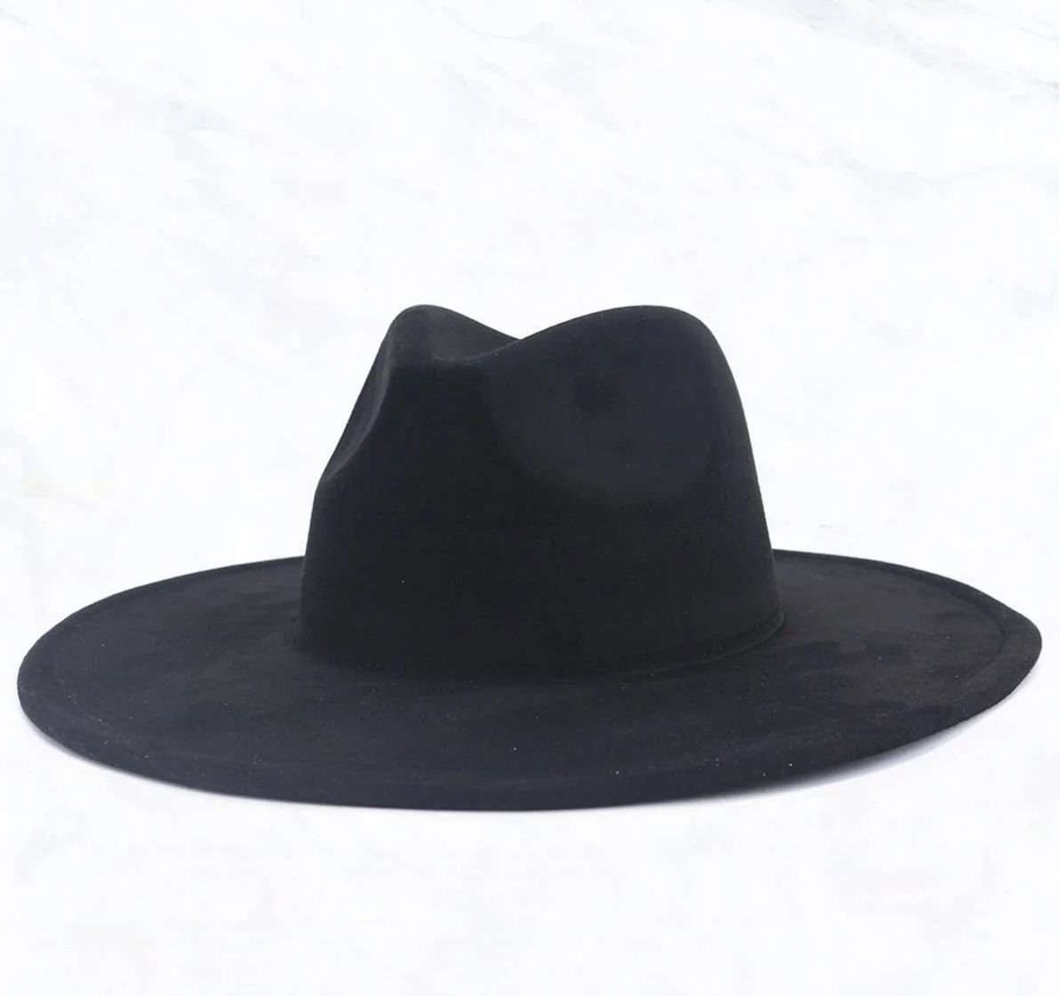 A black fedora hat is sitting on a white surface.