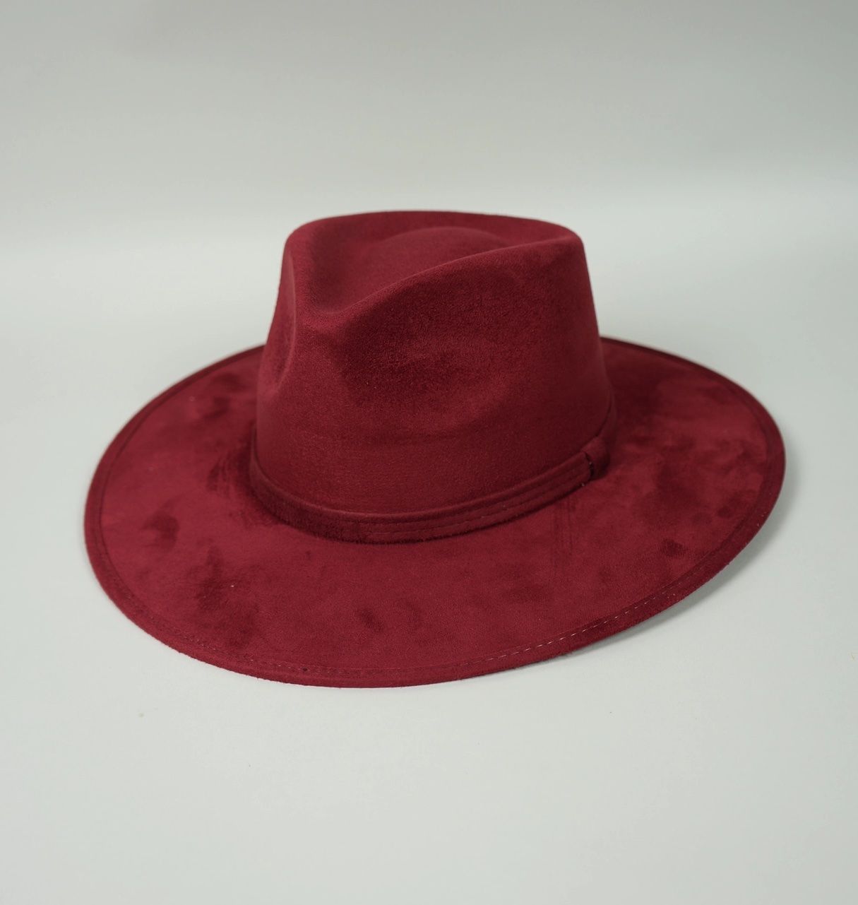 A burgundy fedora hat is sitting on a white surface