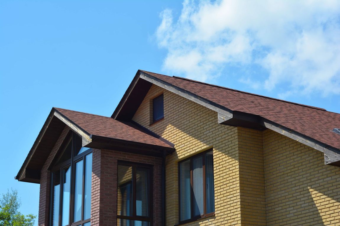 Brick house roof with brown shingles against a blue sky