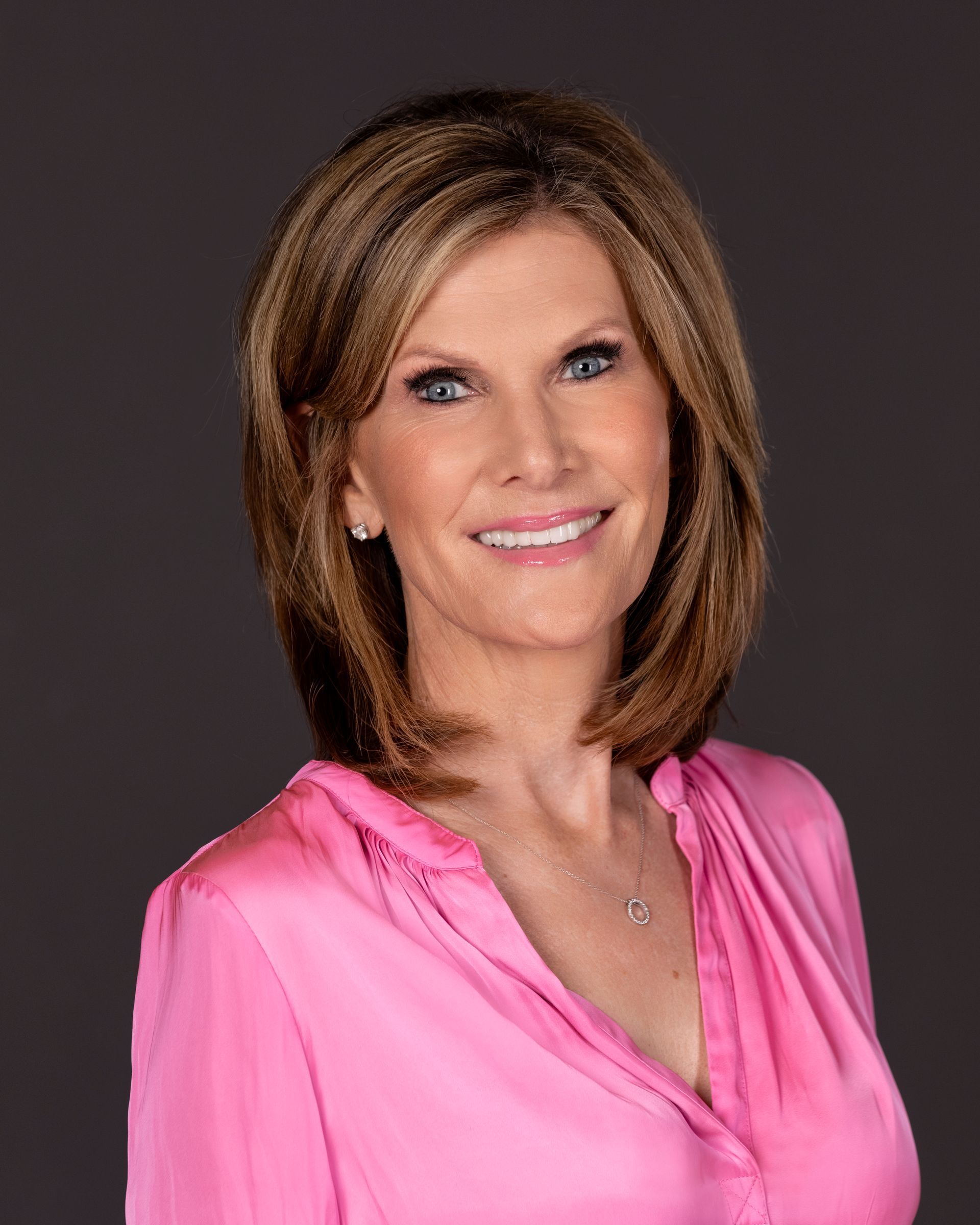 A woman in a pink shirt is smiling for the camera.