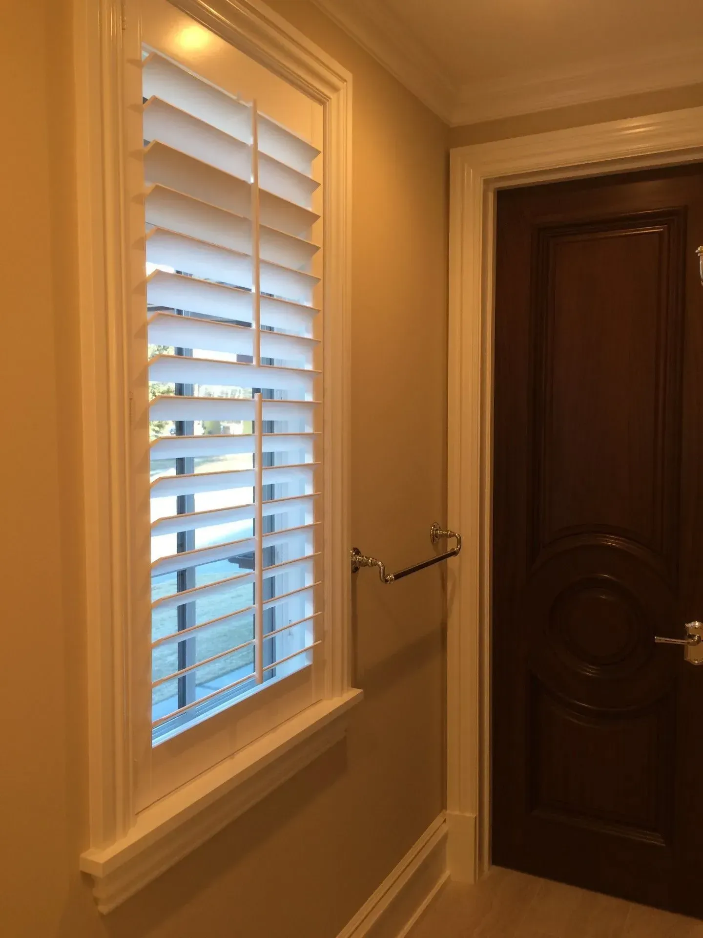 A window with shutters on it is in a hallway next to a door.