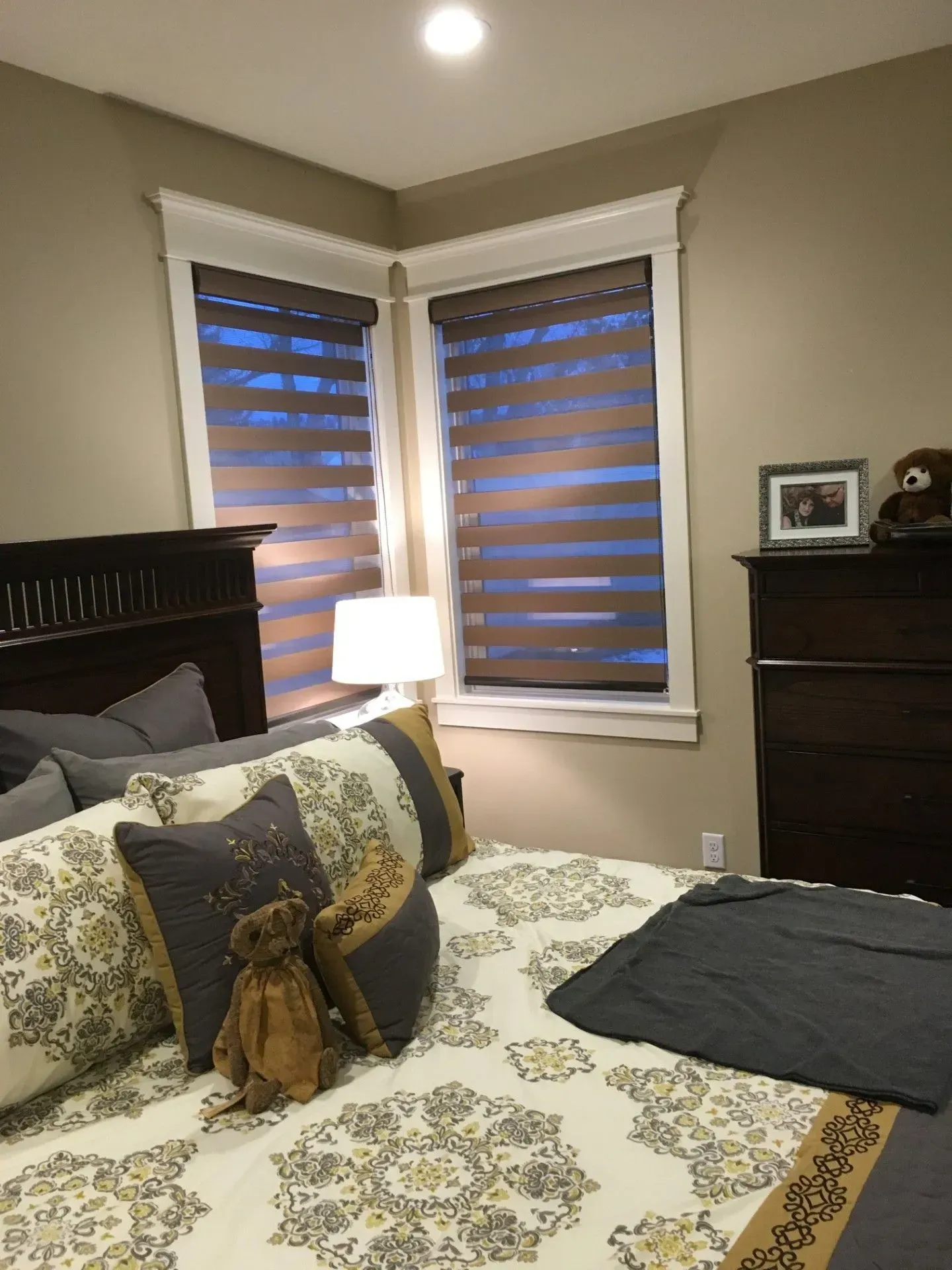 A bedroom with a bed, dresser, lamp and two windows.