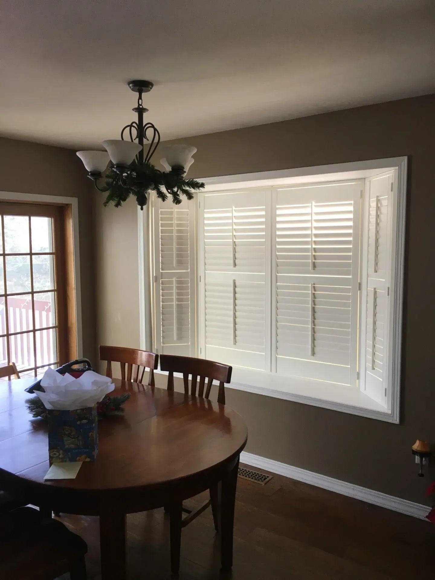 A dining room with a table and chairs and a large window with shutters.