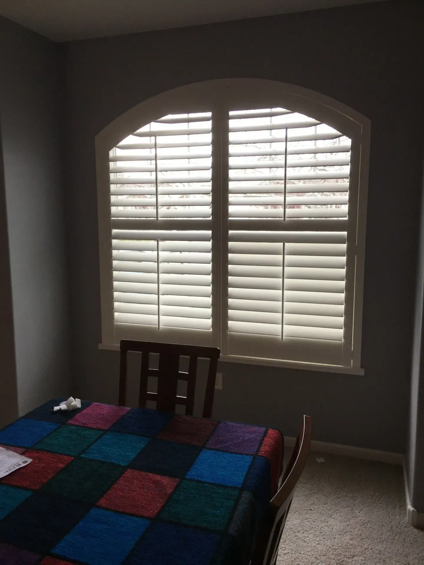 A dining room with a table and chairs and a window with shutters