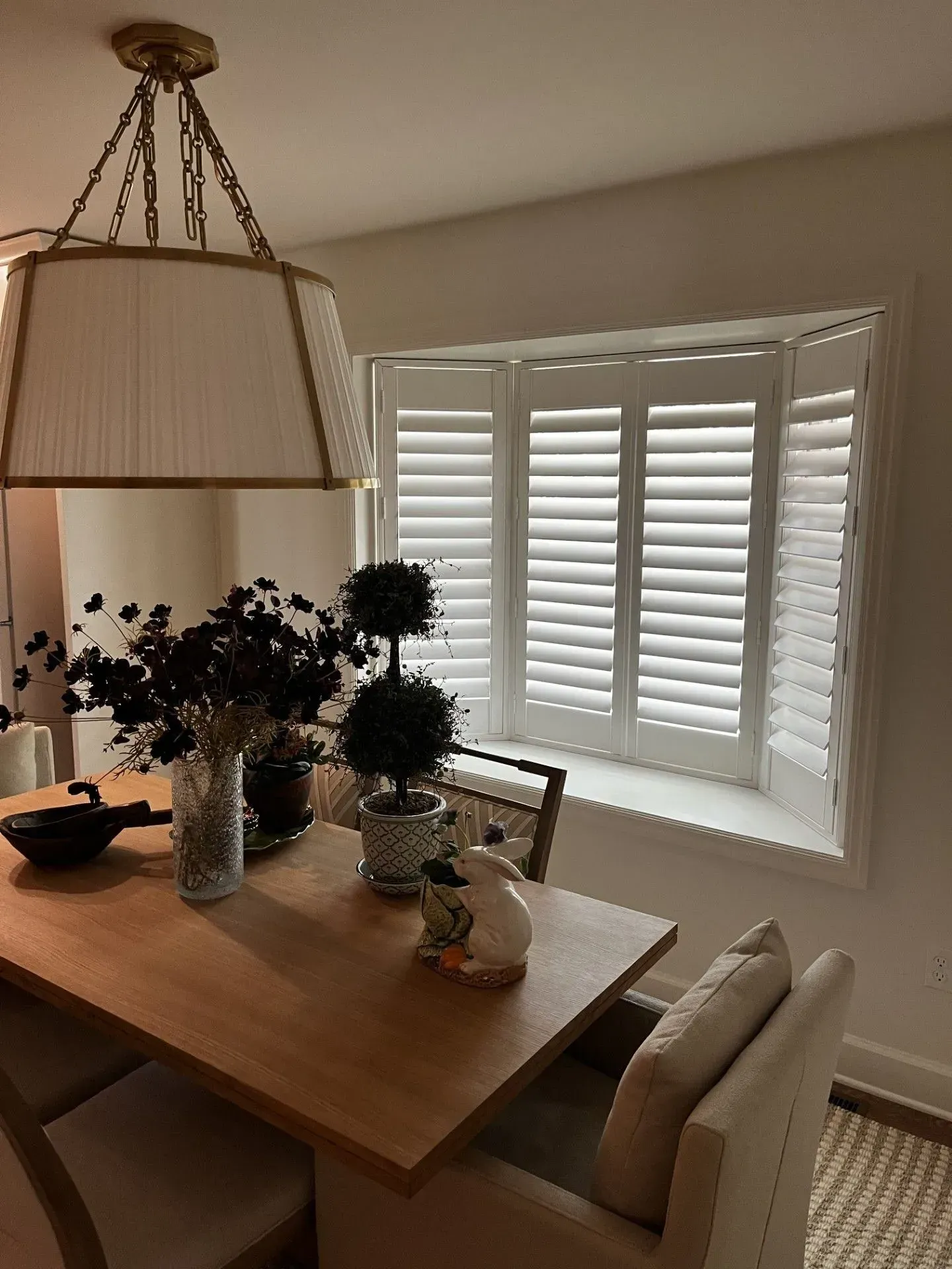 A dining room with a table and chairs and shutters on the windows.