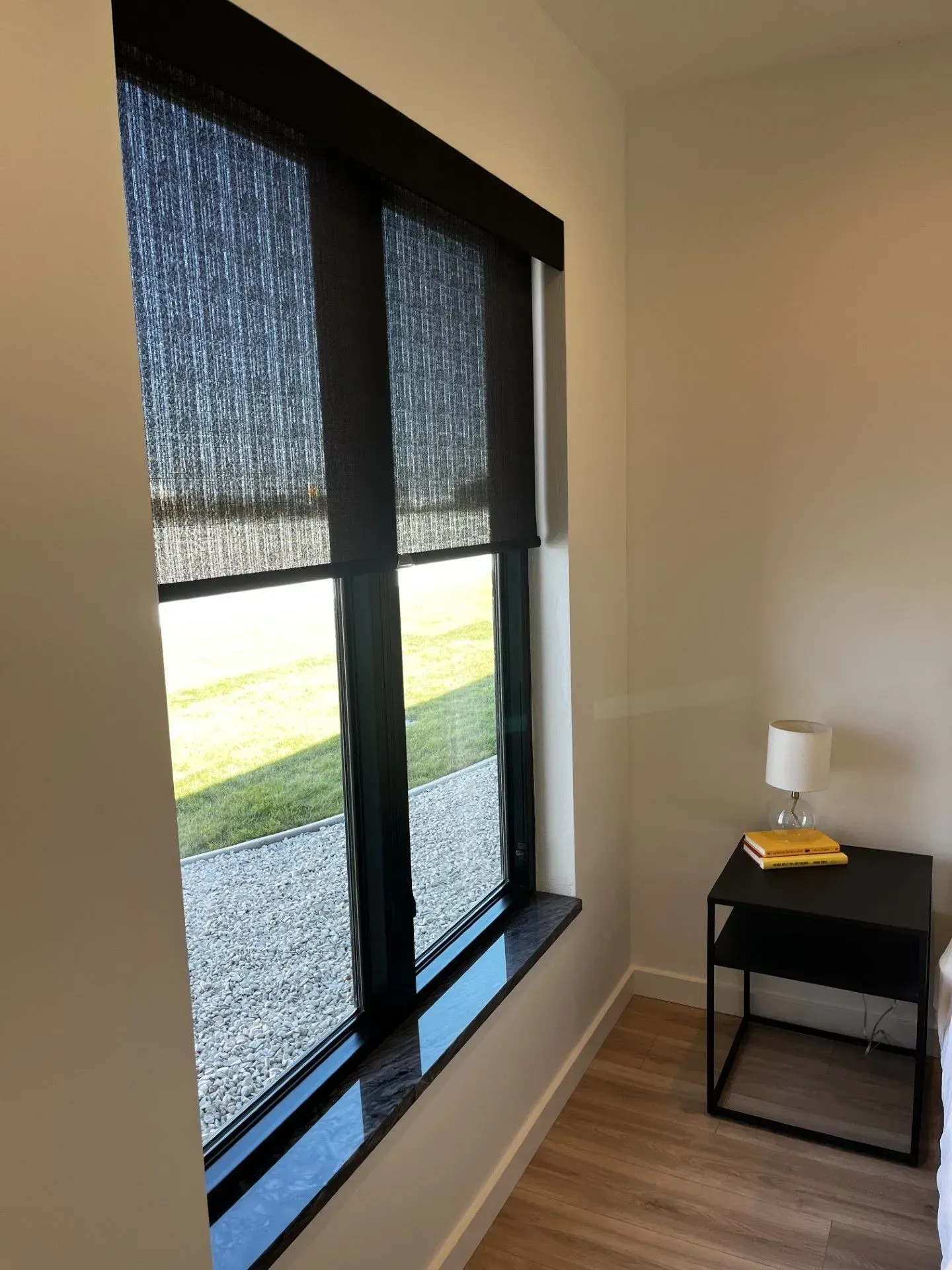 A bedroom with two windows, a nightstand and a lamp.