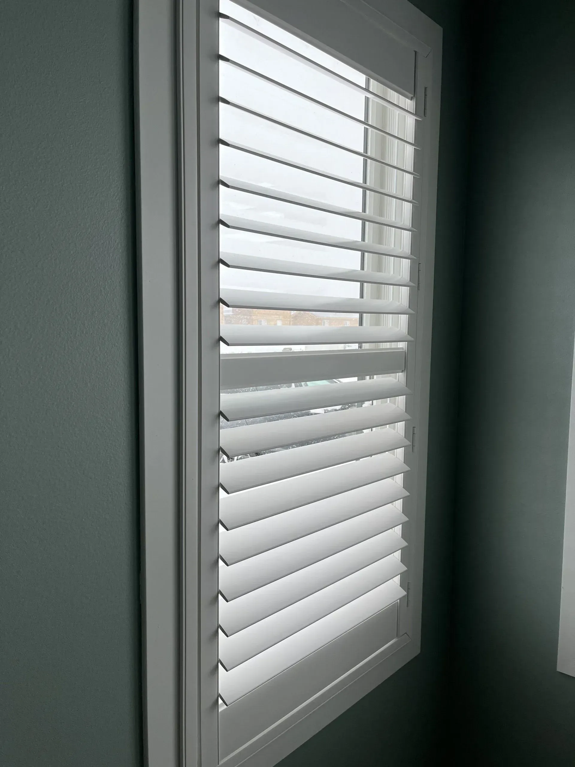 A window with white shutters on it in a room
