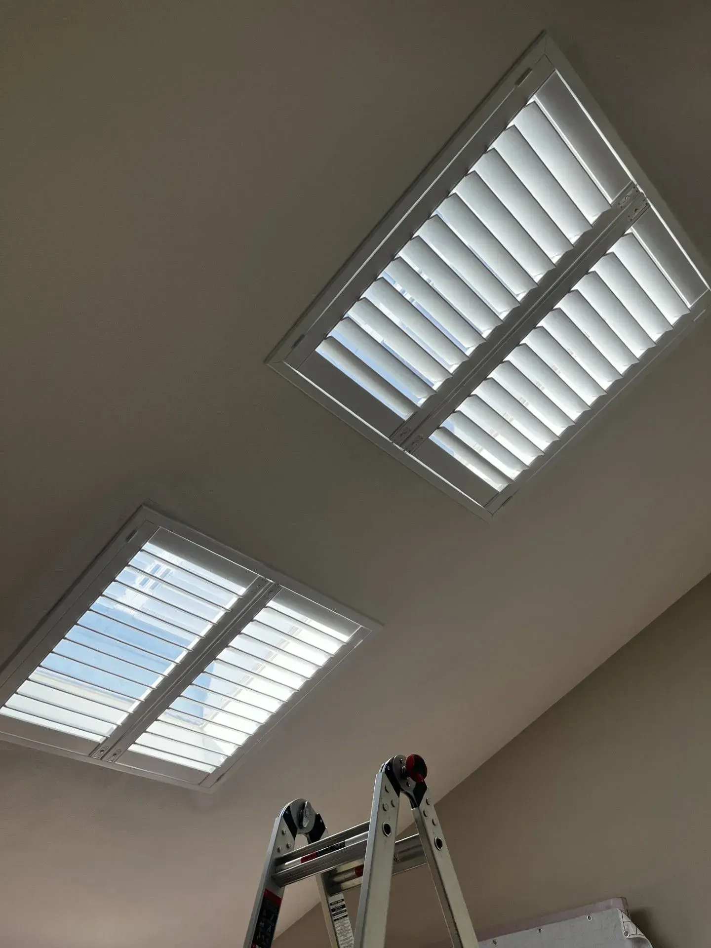 A ladder is sitting under a window with shutters on it.