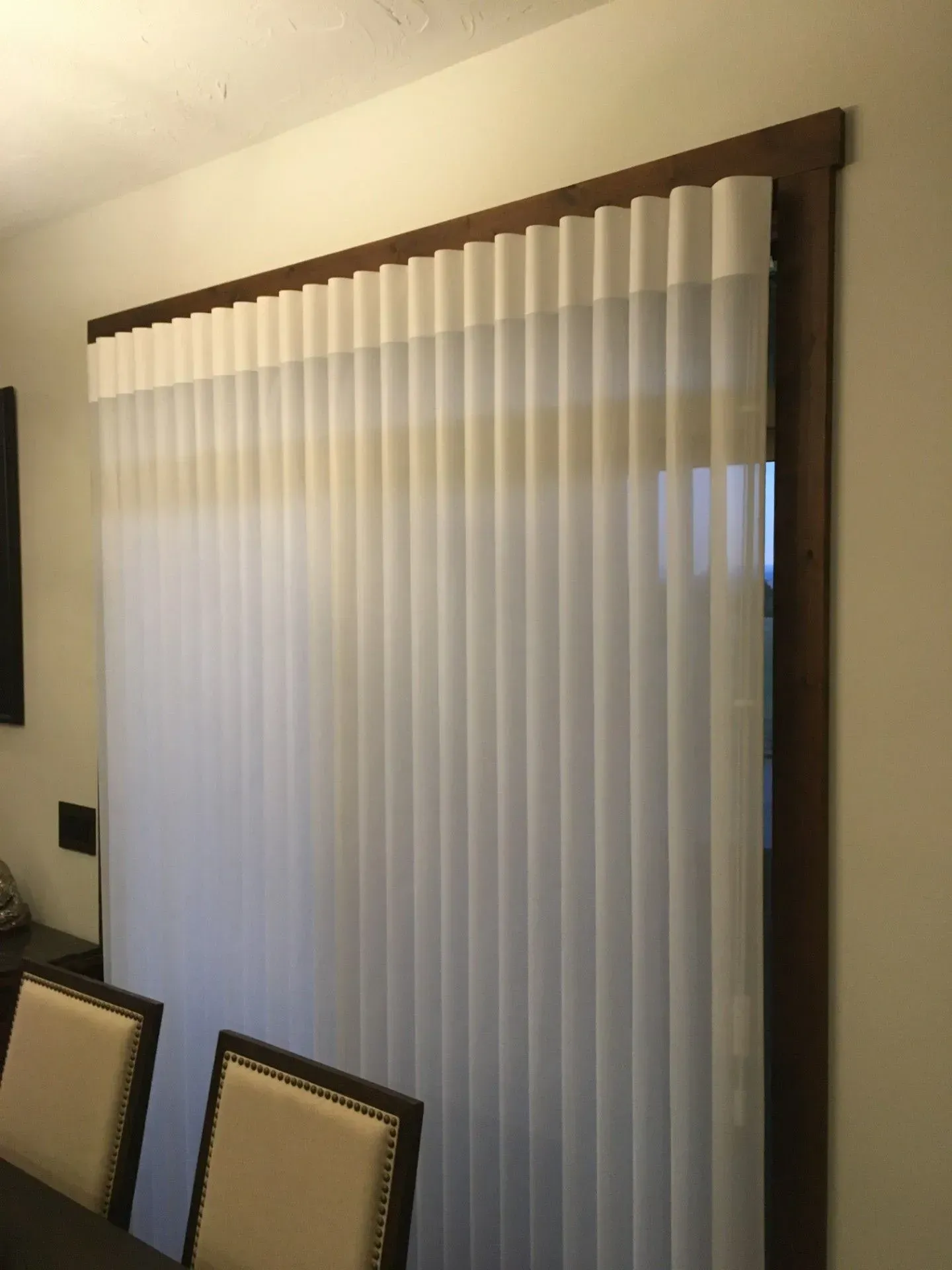 A dining room with a table and chairs and a window with vertical blinds.