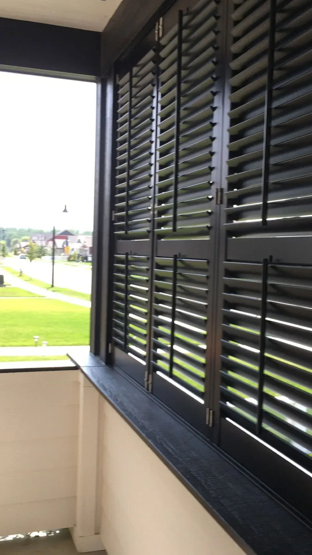 A window with black shutters on it and a view of a field.