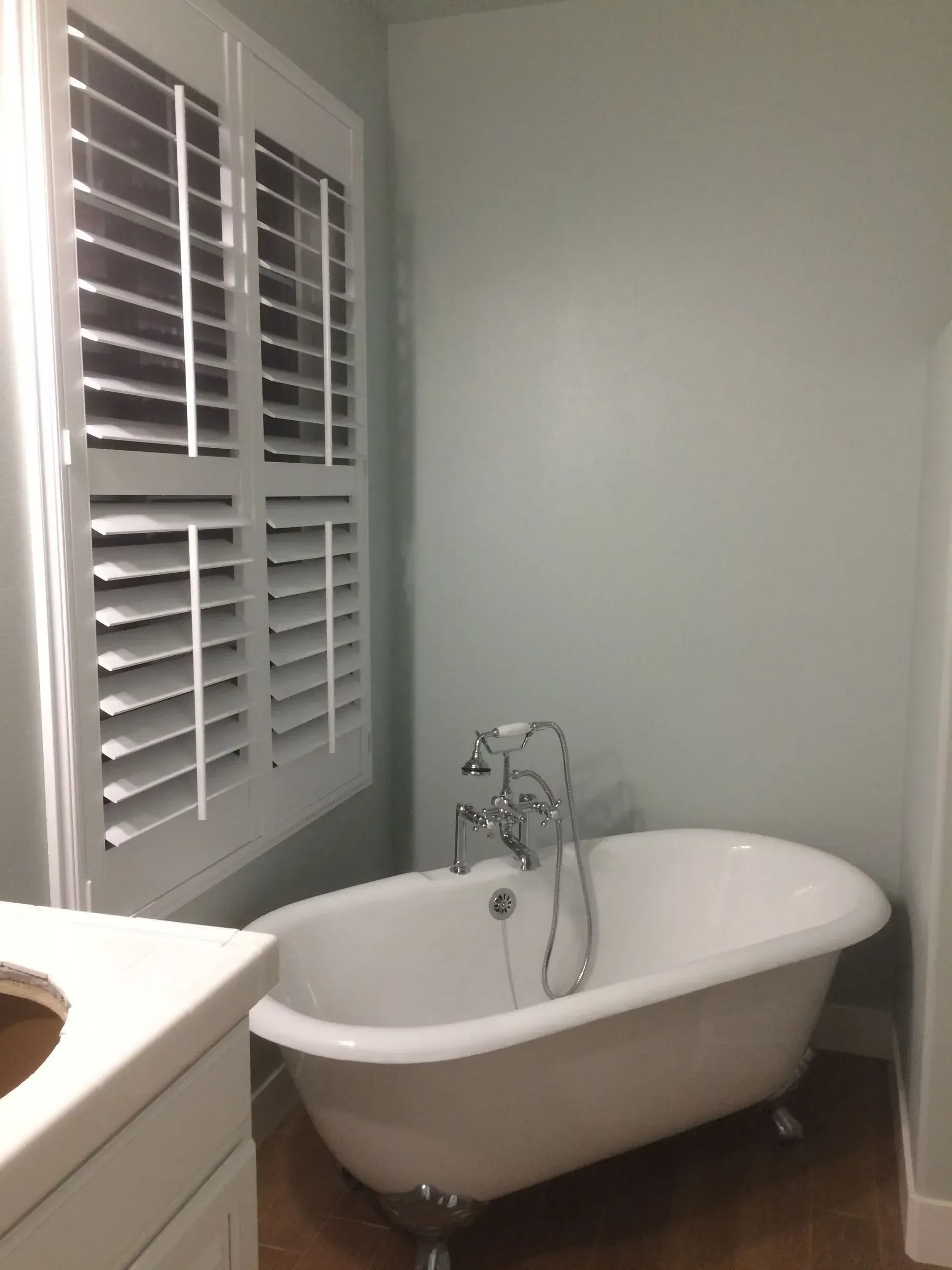 A bathroom with a bathtub and shutters on the window