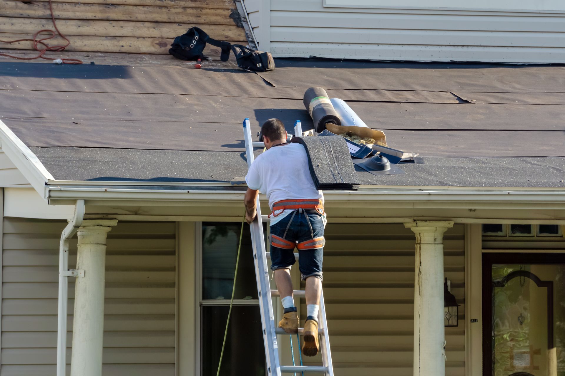 Roofer climbing ladder onto residential roof during shingle replacement. Roofer climbing ladder onto residential roof during shingle replacement.