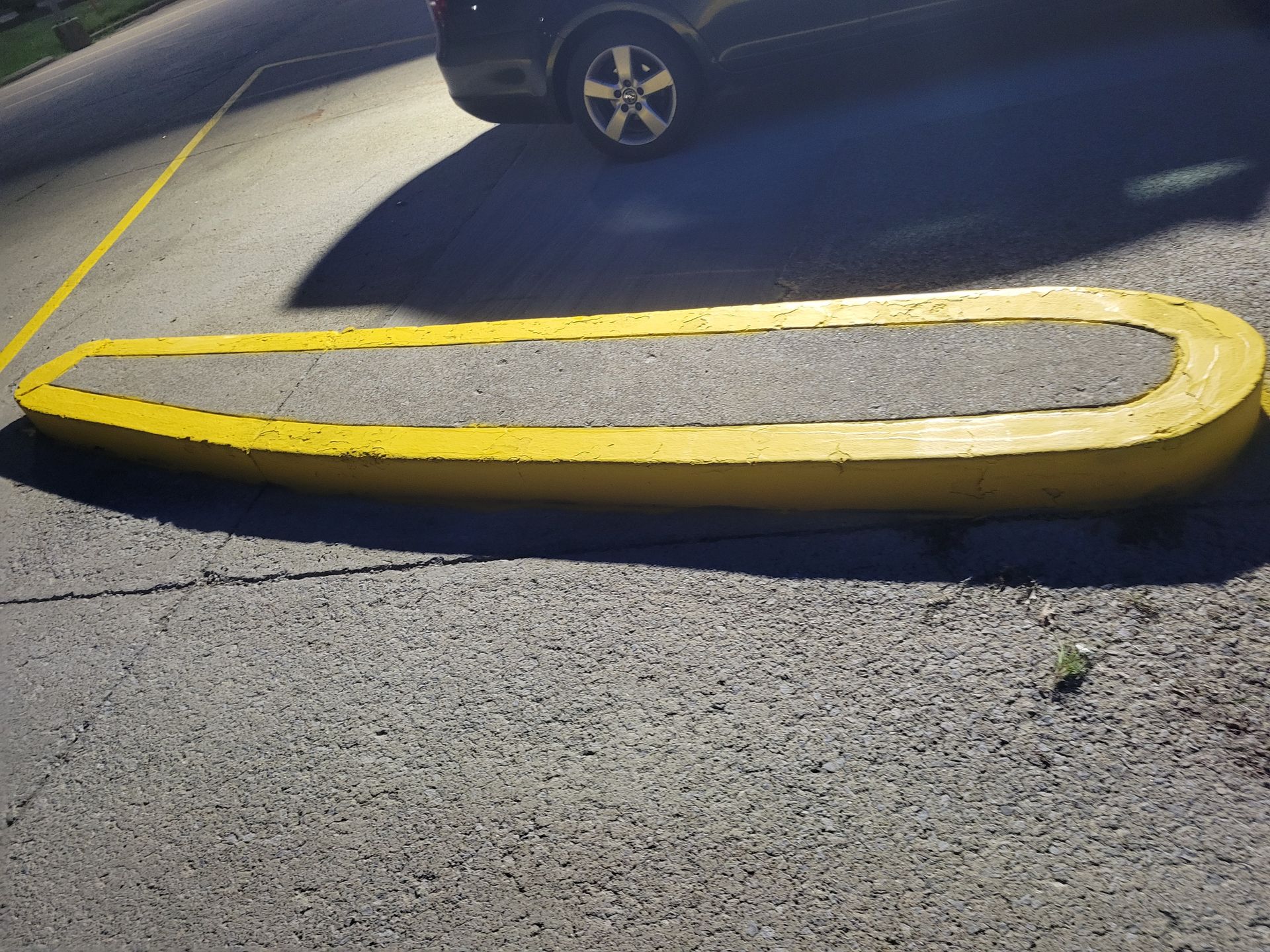 Yellow concrete parking curb in a parking lot, under a black car.