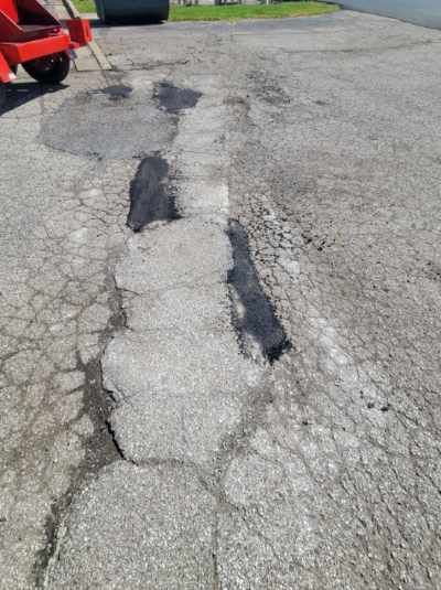 A close up of a cracked asphalt road with a red truck in the background.