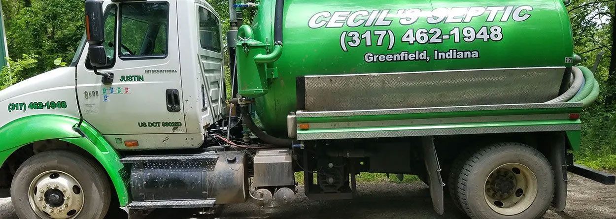 A green and white septic truck is parked on the side of the road.