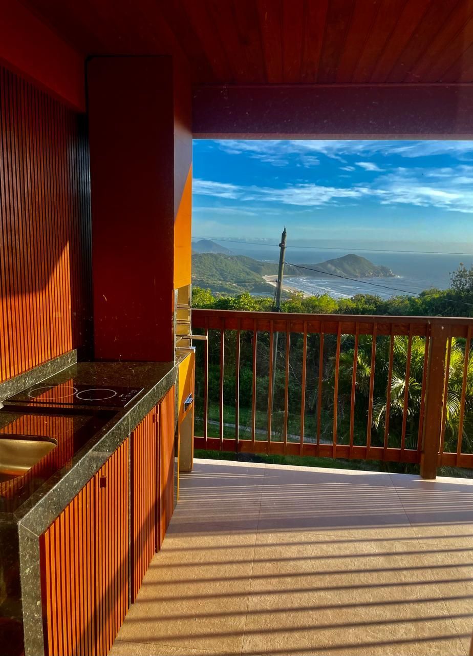 Cozinha externa moderna com armários de madeira e bancada de pedra, com vista para uma paisagem exuberante e o litoral ao longe.
