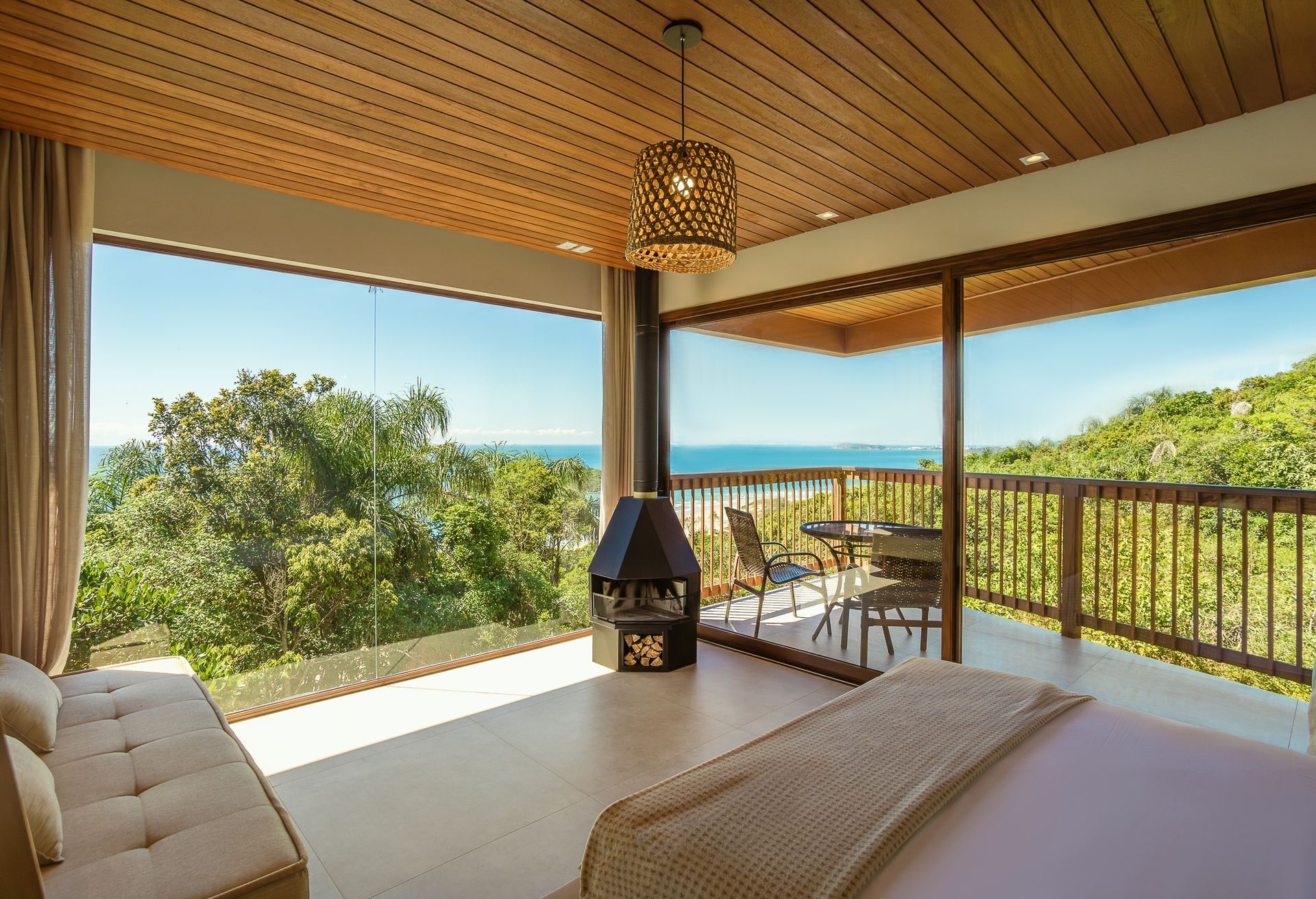Um quarto luxuoso com vista panorâmica para o oceano, com teto de madeira, lareira central e varanda privativa.