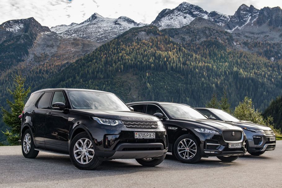 Three black cars are parked in front of a mountain.