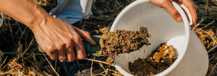Hand with small shovel putting dirt in a bucket. 