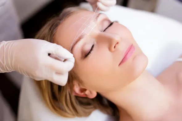 Person bei Wimpernlifting; Creme wird mit einem Pinsel auf die Wimpern aufgetragen. Augenklappe angelegt.