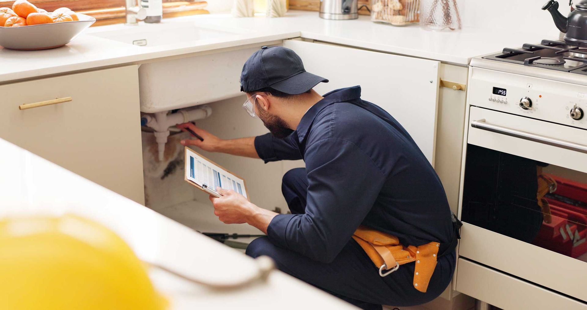 Person kneels in a kitchen, checking under a white cabinet near a stove and countertop. Person kneels in a kitchen, checking under a white cabinet near a stove and countertop.
