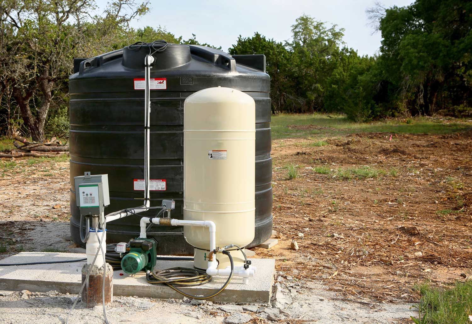 Water pump and two large storage tanks beside a dirt clearing and trees. Water pump and two large storage tanks beside a dirt clearing and trees.