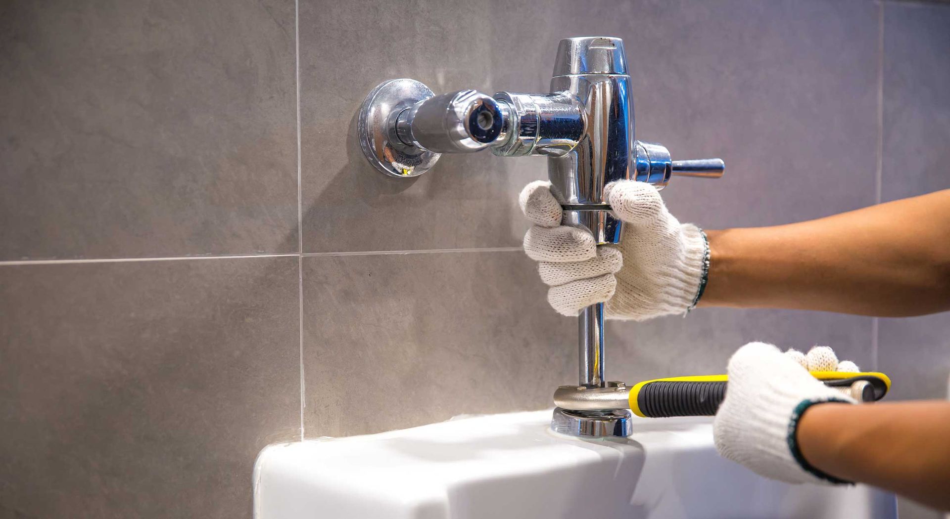 Gloved hands repairing a bathroom faucet with a wrench over a white sink.
