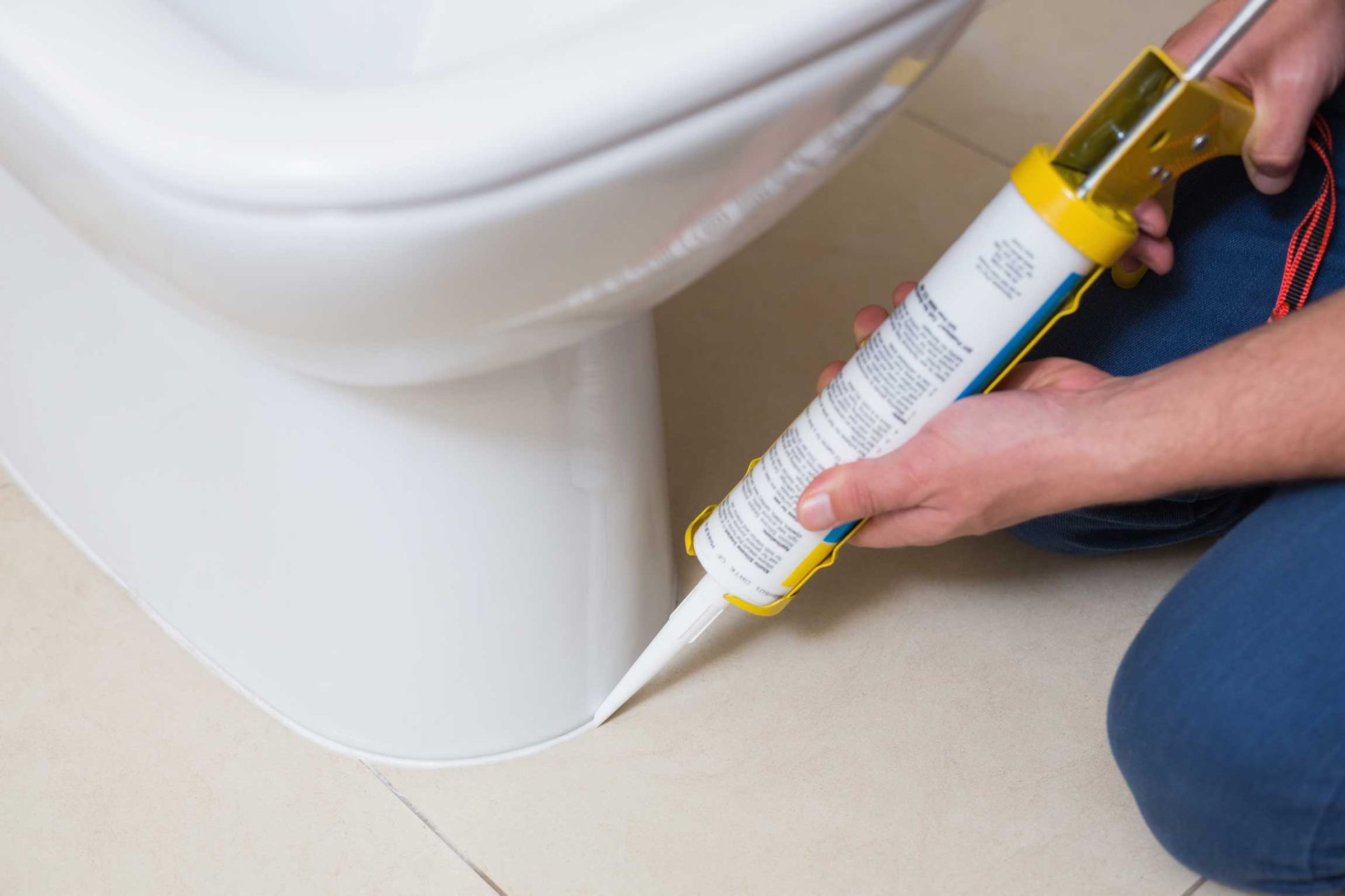 Applying caulk around the base of a white toilet with a caulking gun.