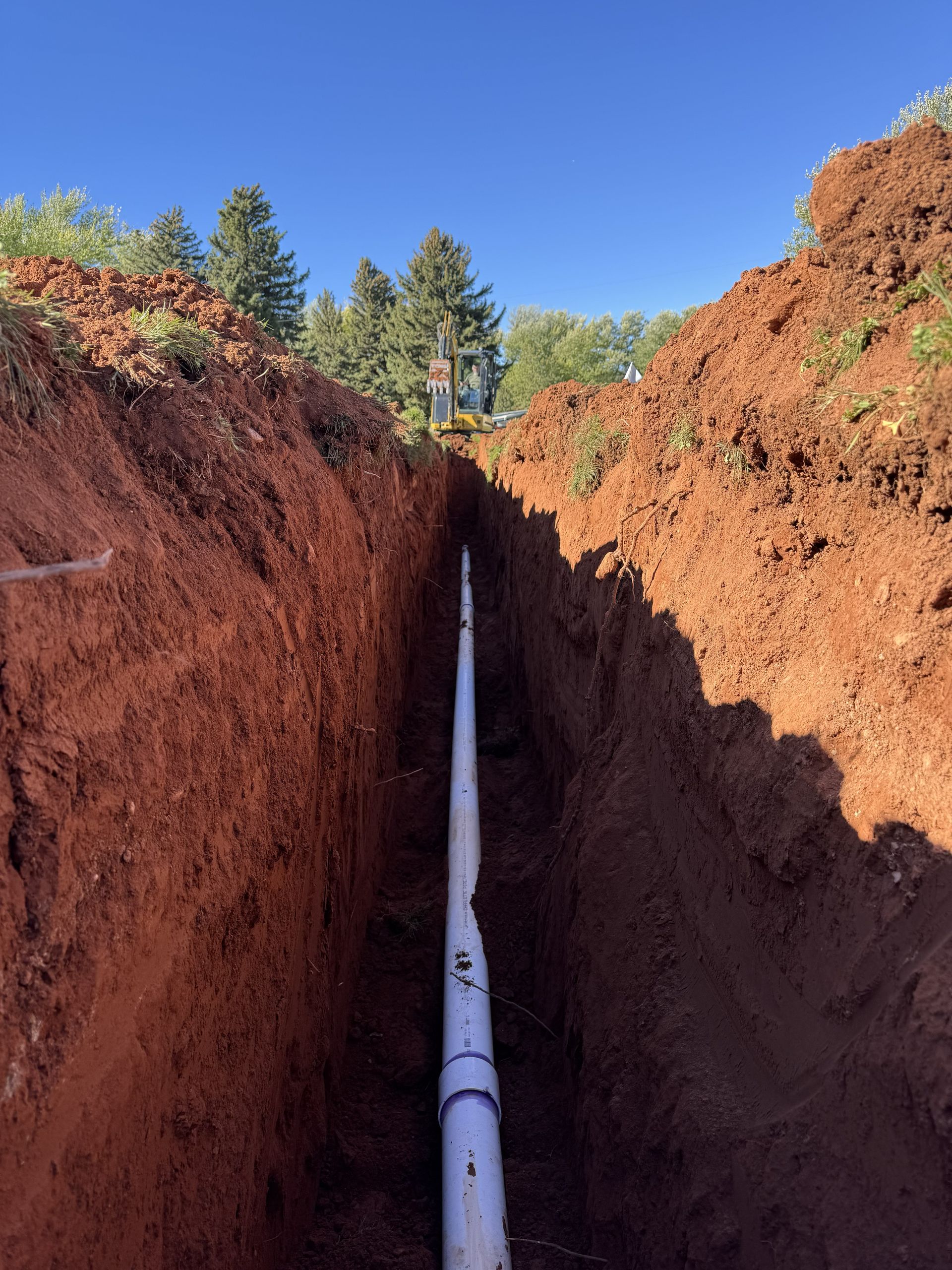 PVC plumbing vent pipe in a dirt trench beside a brick wall and exposed utility lines