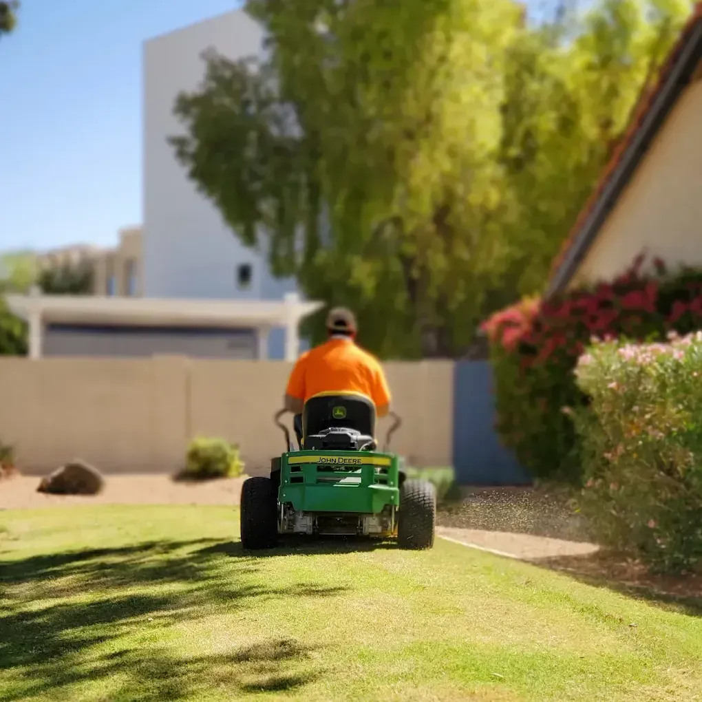 A man is riding a green lawn mower on a lush green lawn.
