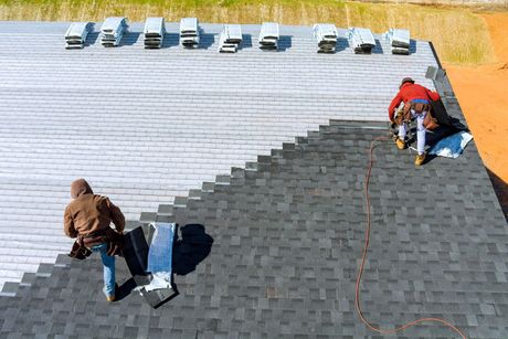 Two roofers installing shingles on a roof, transitioning from light to dark grey.