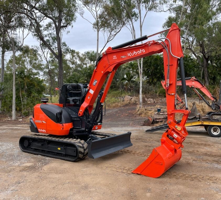 An Orange Excavator is Digging a Hole in a Field — Eddy’s Excavations & Bobcat Hire In Boyne Valley, QLD