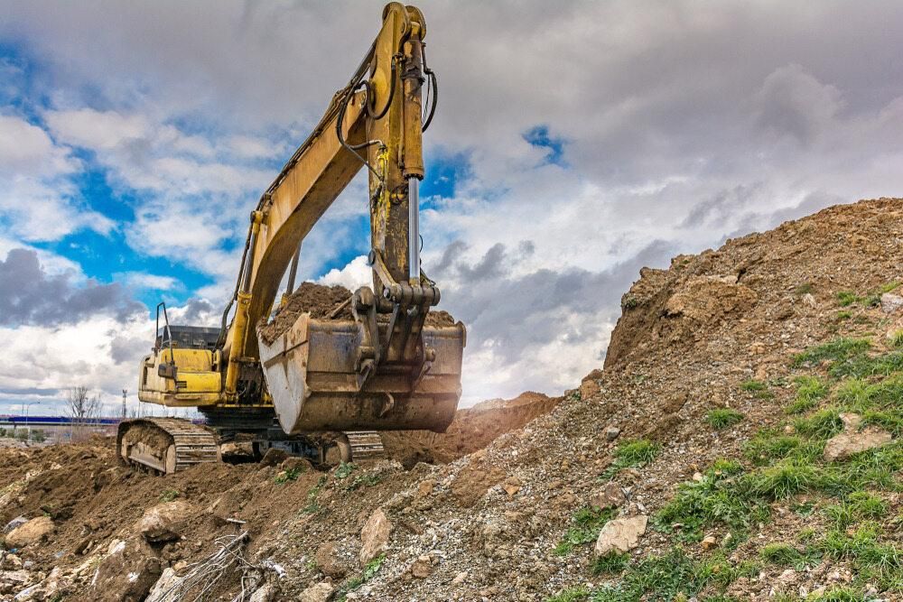 A Yellow Excavator is Digging a Pile of Dirt on a Hill — Eddy’s Excavations & Bobcat Hire In Biloela, QLD