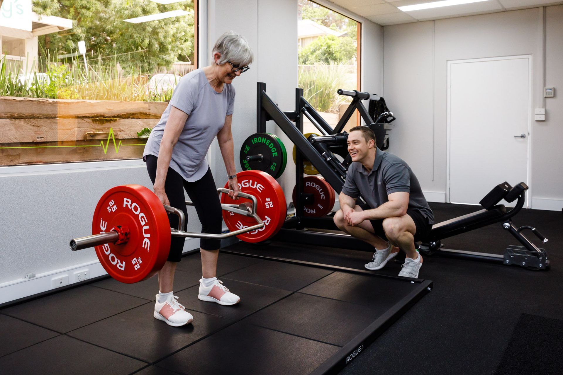 A man is squatting next to a woman lifting a barbell in a gym.